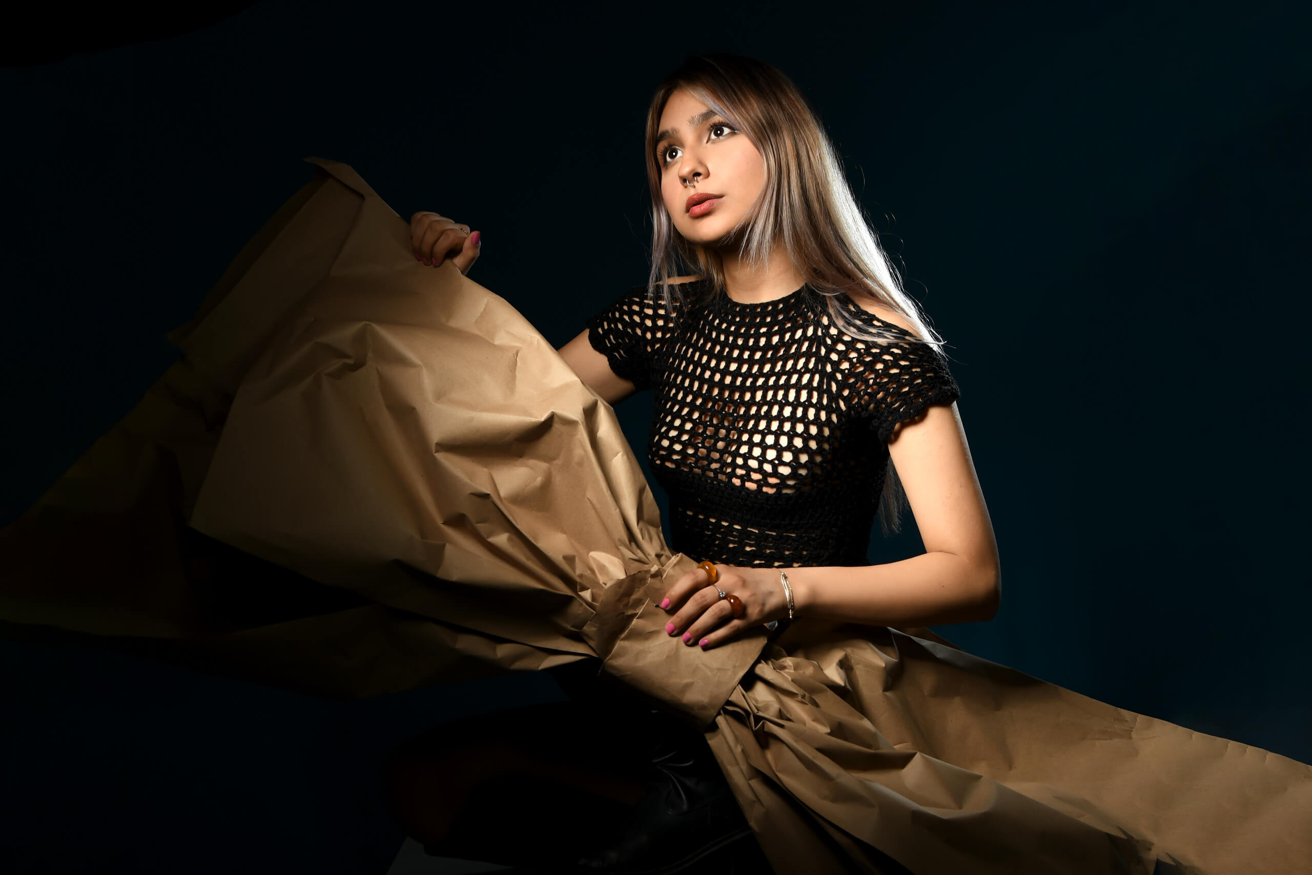Sesión de fotos creativa en estudio con joven vistiendo top negro tejido y sosteniendo papel kraft gigante