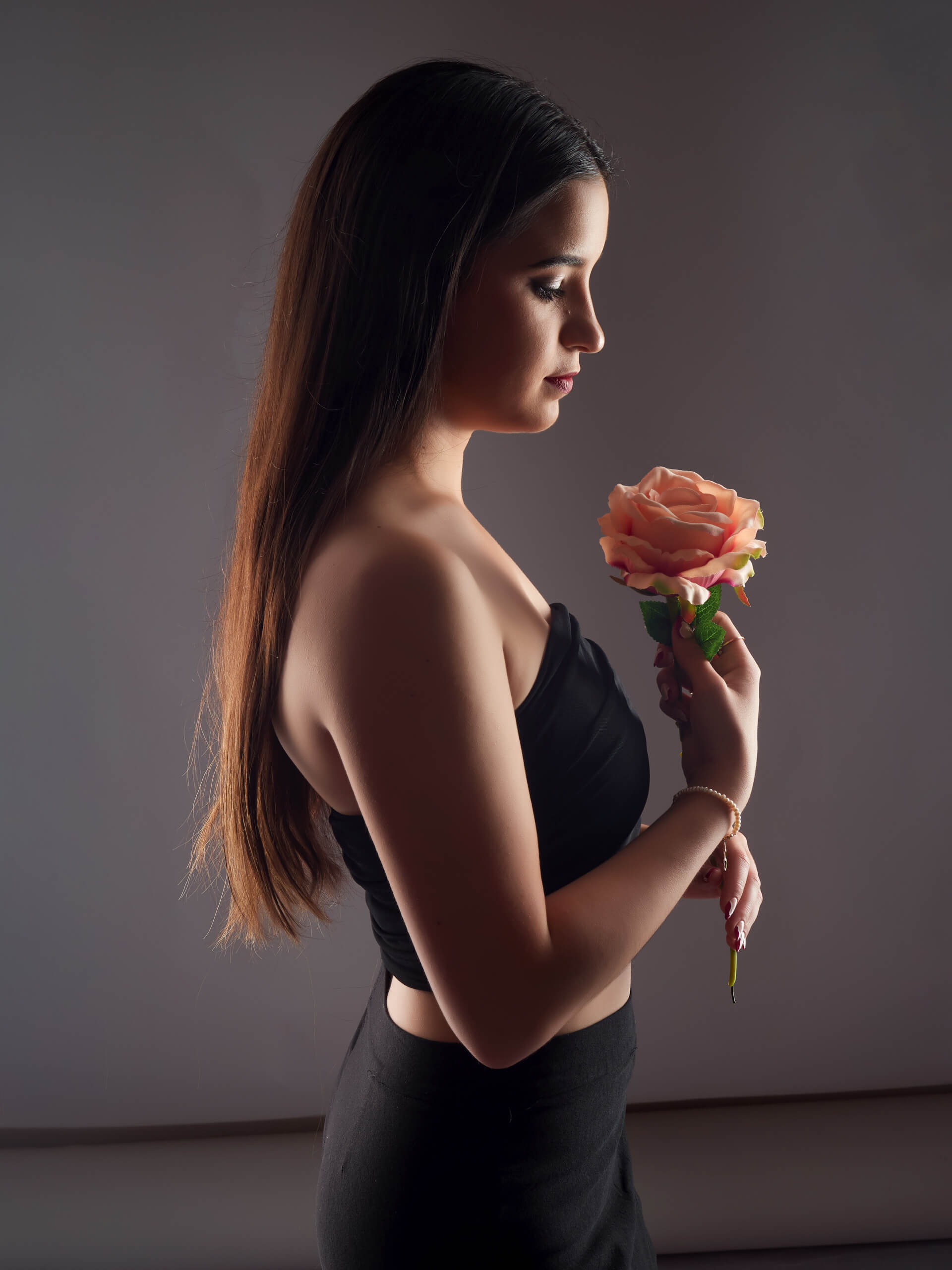 Retrato artístico de perfil en clave baja de joven de cabello largo sosteniendo una rosa color salmón